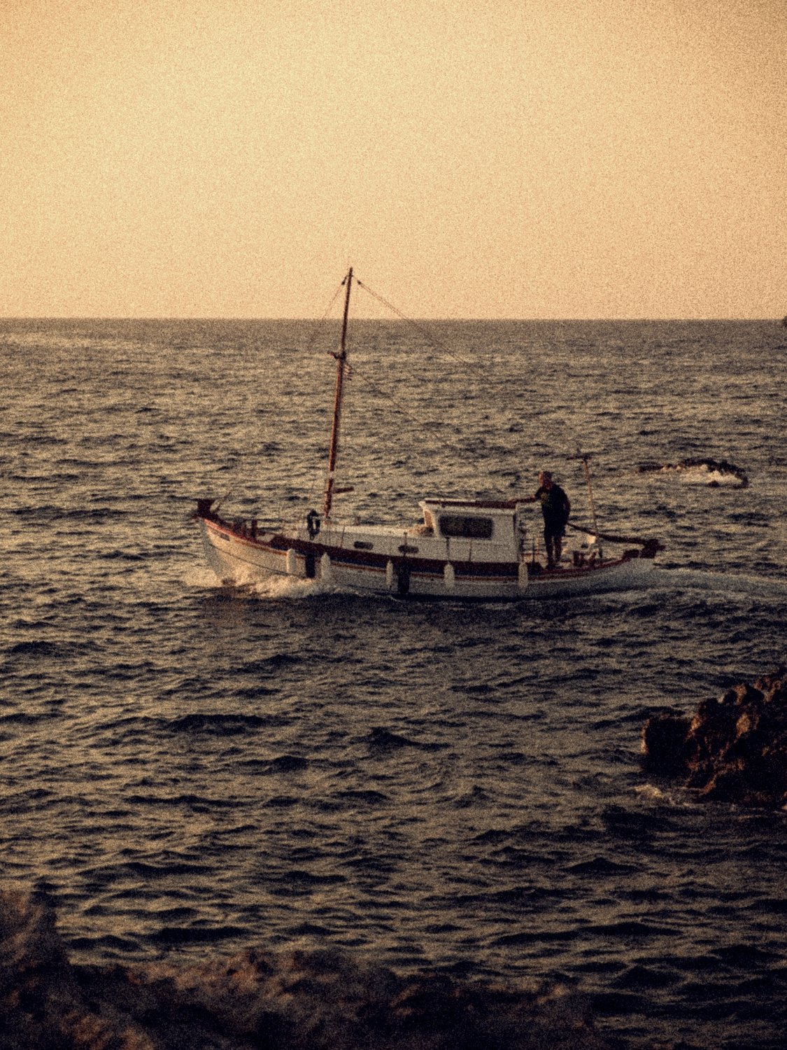 A traditional fishing boat heading out at sunset