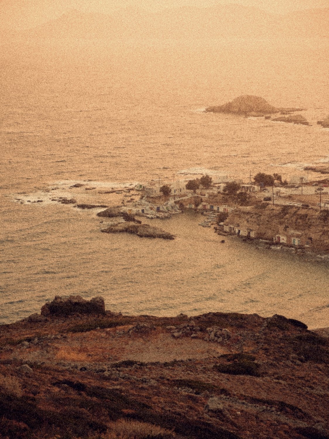 Mandrakia from the hillside at dusk: the village and its boathouses on the bay, the islets beyond