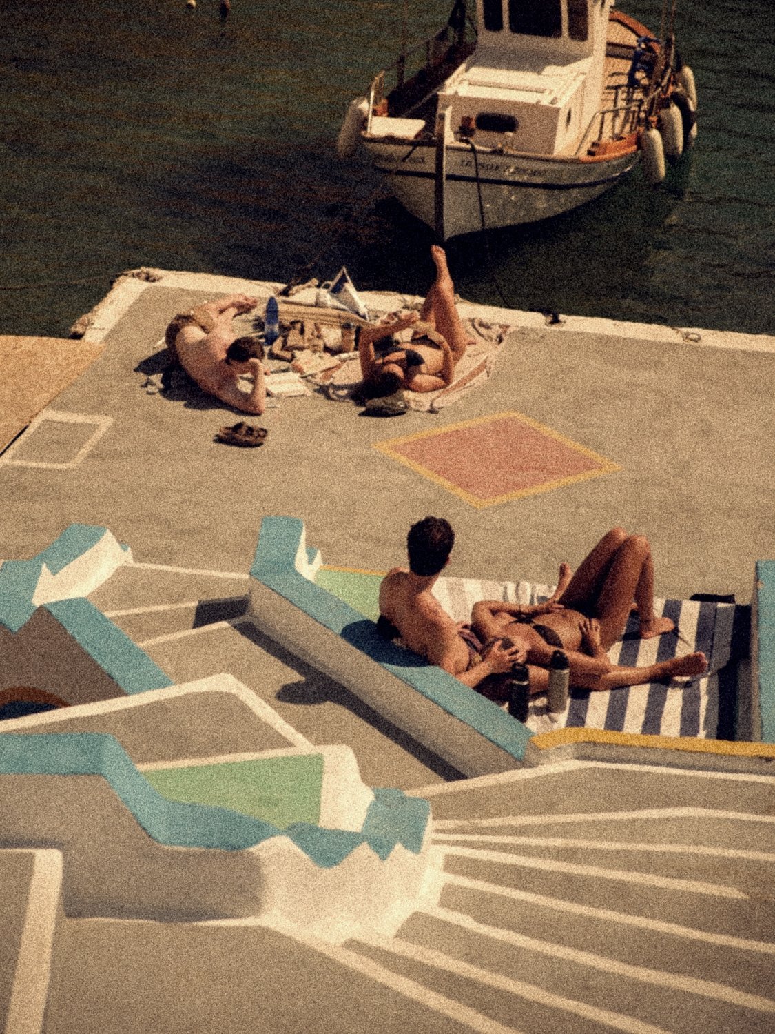 Sunbathers on the painted steps and quay above a moored fishing boat